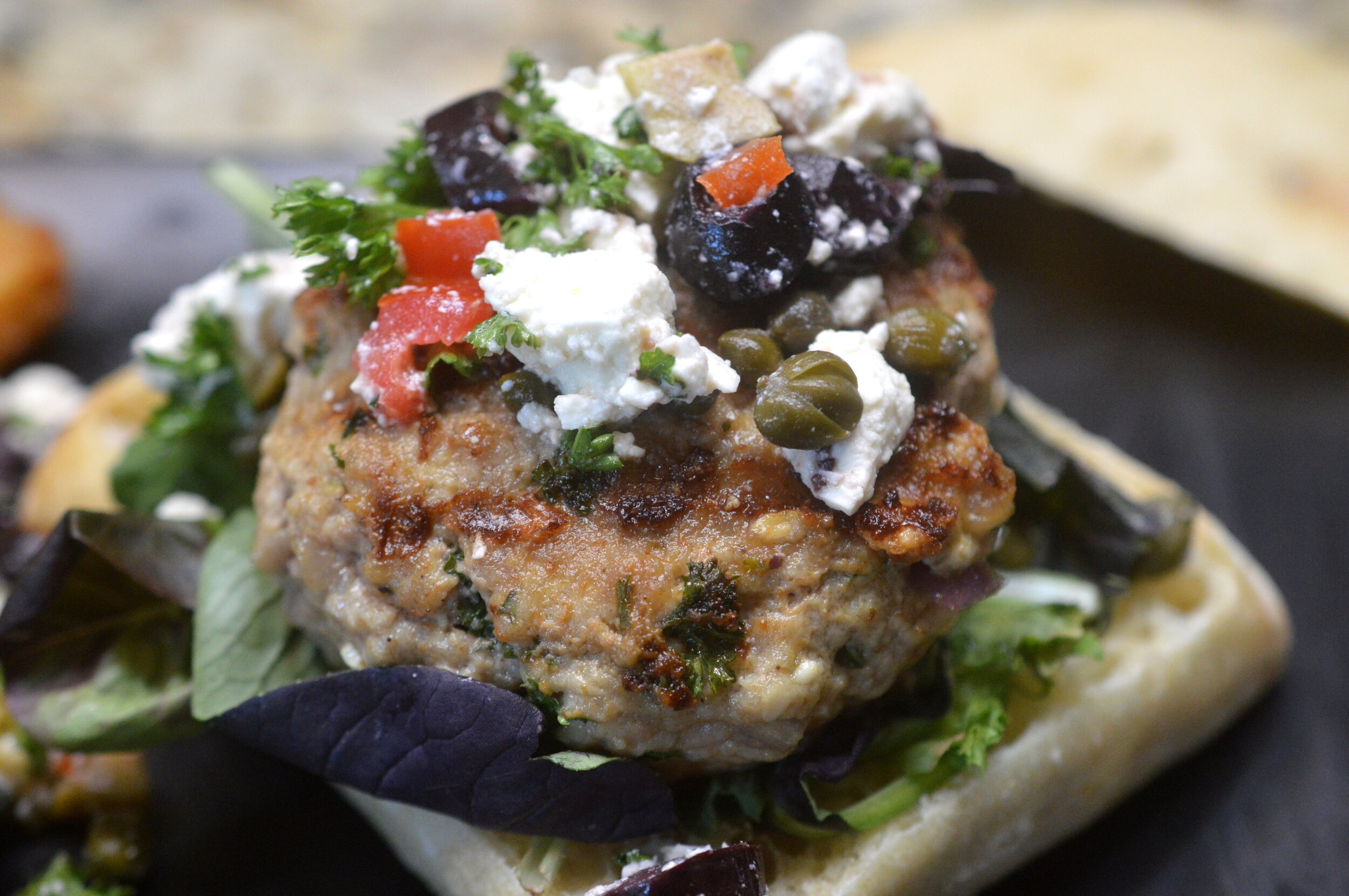 Open faced Veal Mediterranean burger topped with feta cheese, olives, dill, and capers