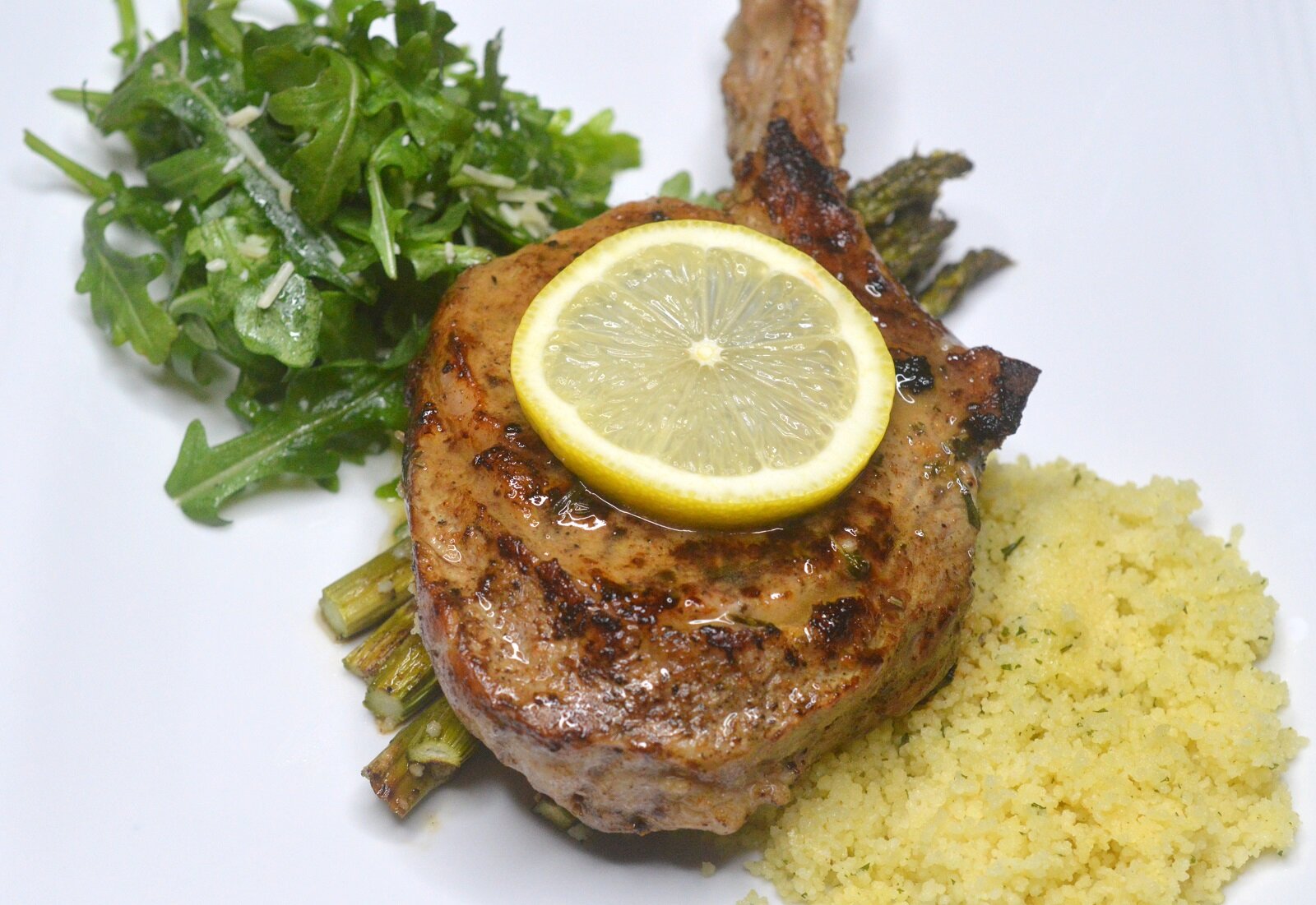 Pan seared veal chops with a side of arugula and rice topped with a slice of lemon.