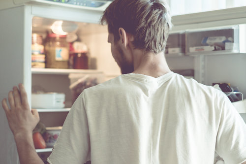 young handsome bearded man standing near opended fridge at home kitchen
