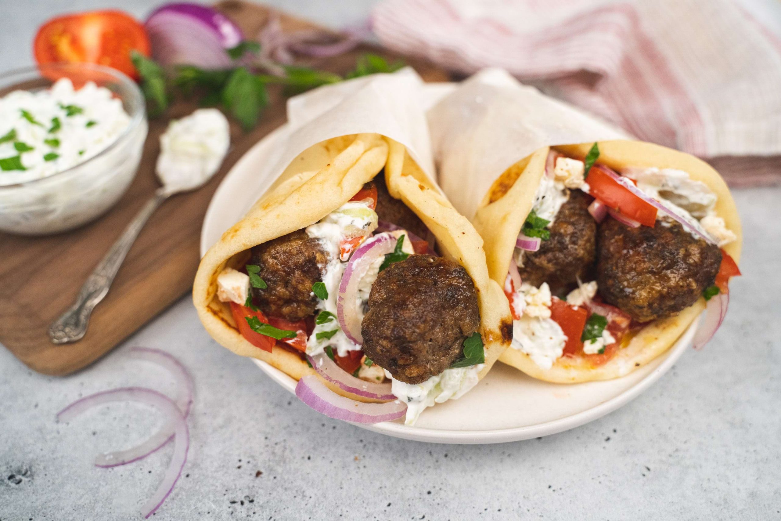 Perfectly grilled meatballs served as a gyro with home made tzatziki, fresh red onion, and a tomato cucumber salad.