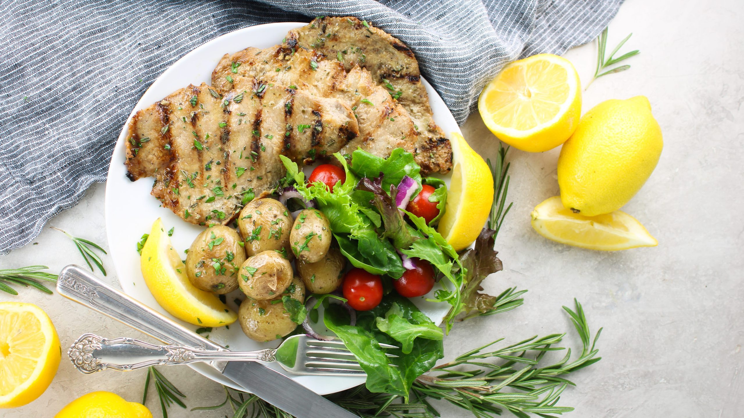 These Rosemary Grilled veal cutlets are season to perfection and served with grill marks over roasted potatoes, and with a side salad and lemon wedges.