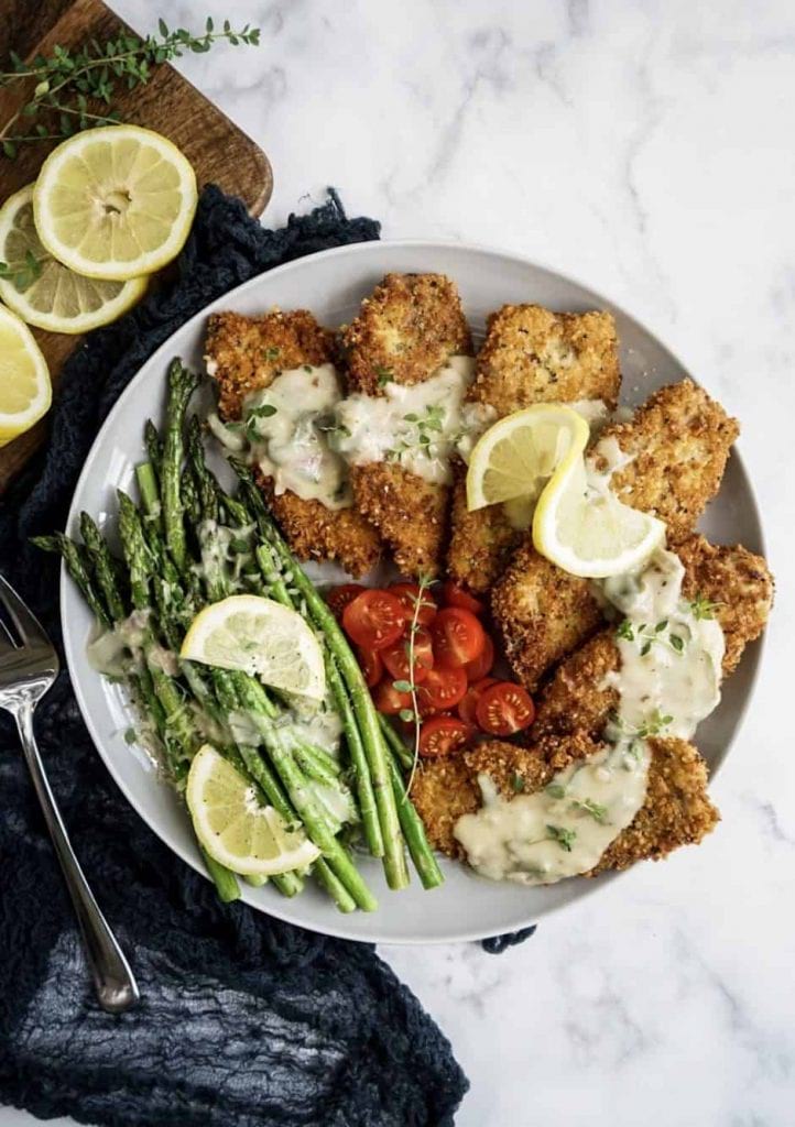 Saltimbocca Milanese topped with a white wine age sauce, served with fresh cooked asparagus, and sliced cherry tomatoes. Lemon for garnish.