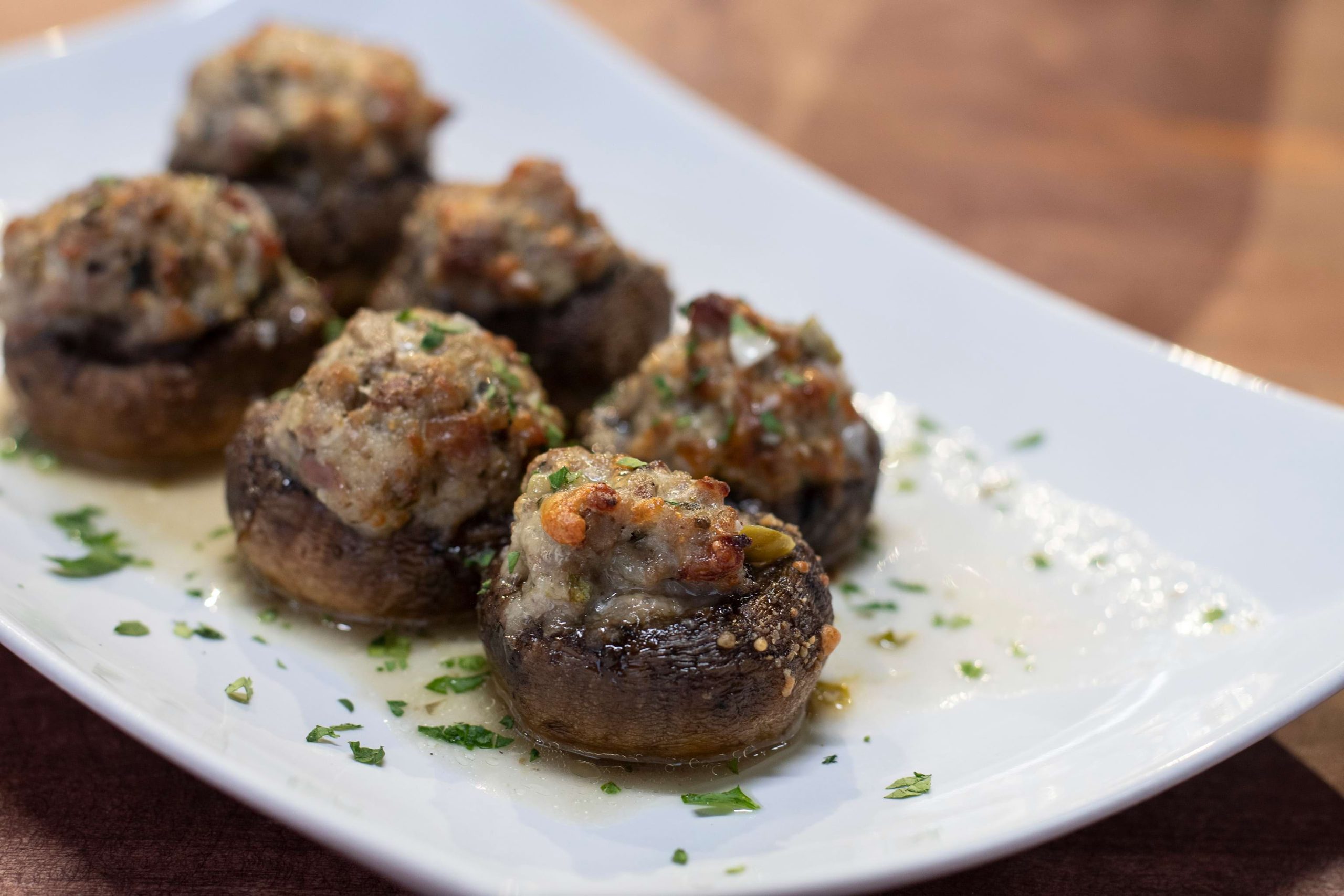 Ground veal mixture stuffed in baby bell mushrooms and cooked to a crispy top, served on a white plated with a light piccata sauce drizzled.