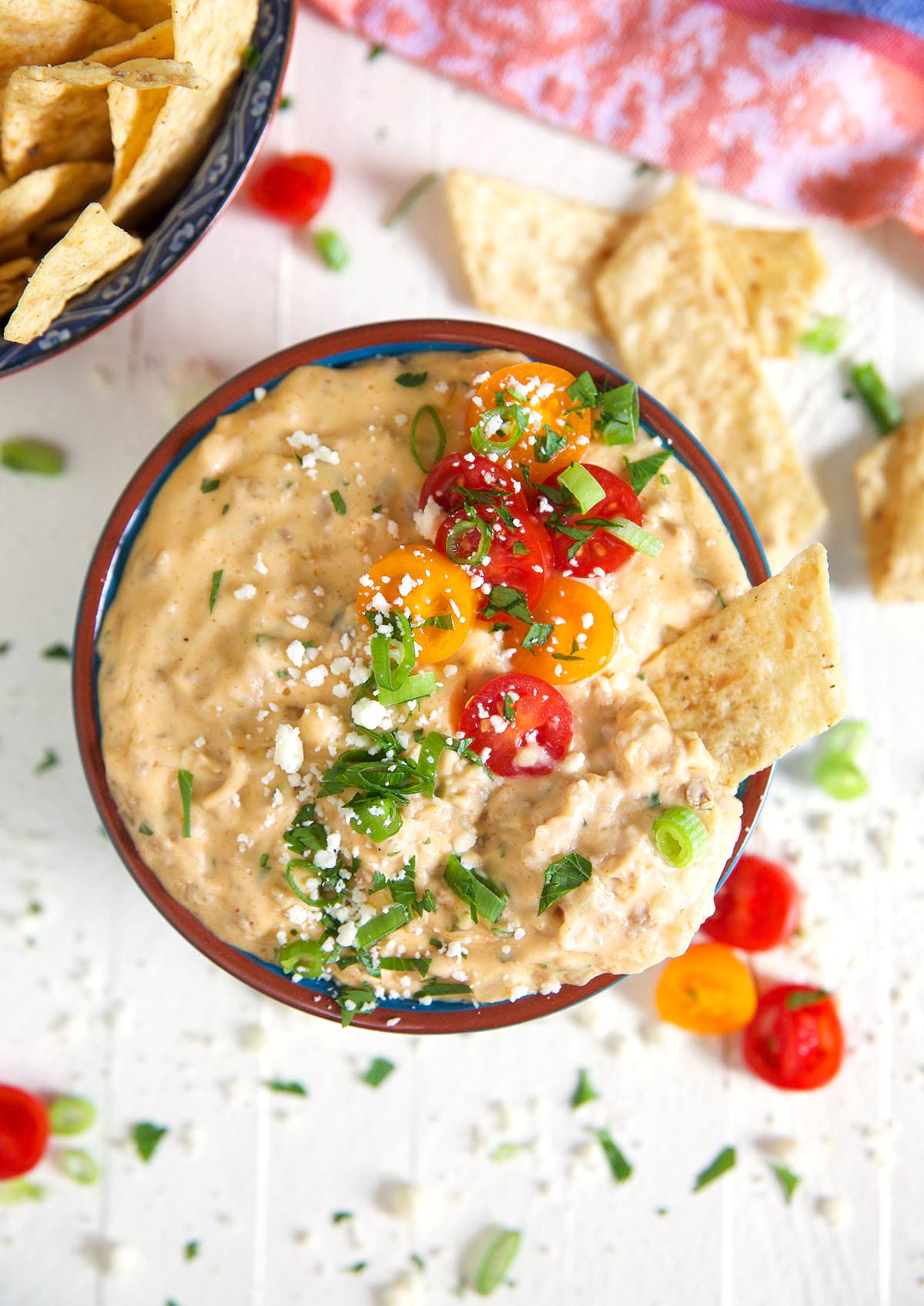 Veal white queso dip in a colorful blue bowl, topped with cheese, and sliced tomatoes top view of dipping bowl