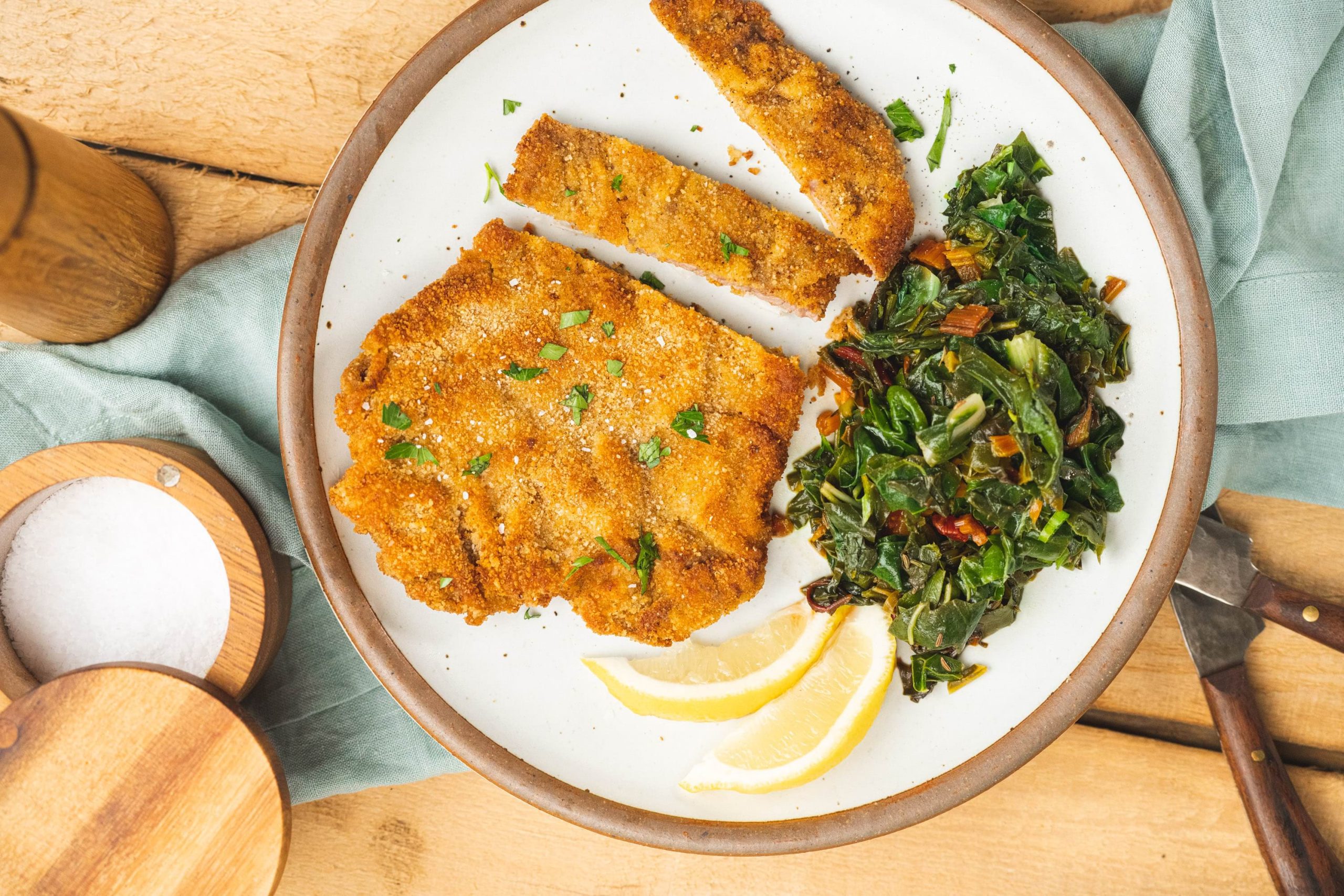 Crispy golden veal schnitzel plated with Swiss Chard rainbow greens and slices of fresh lemon