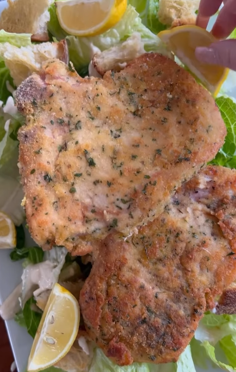 Classic Veal Milanese atop fresh salad and drizzled with lemon juice.