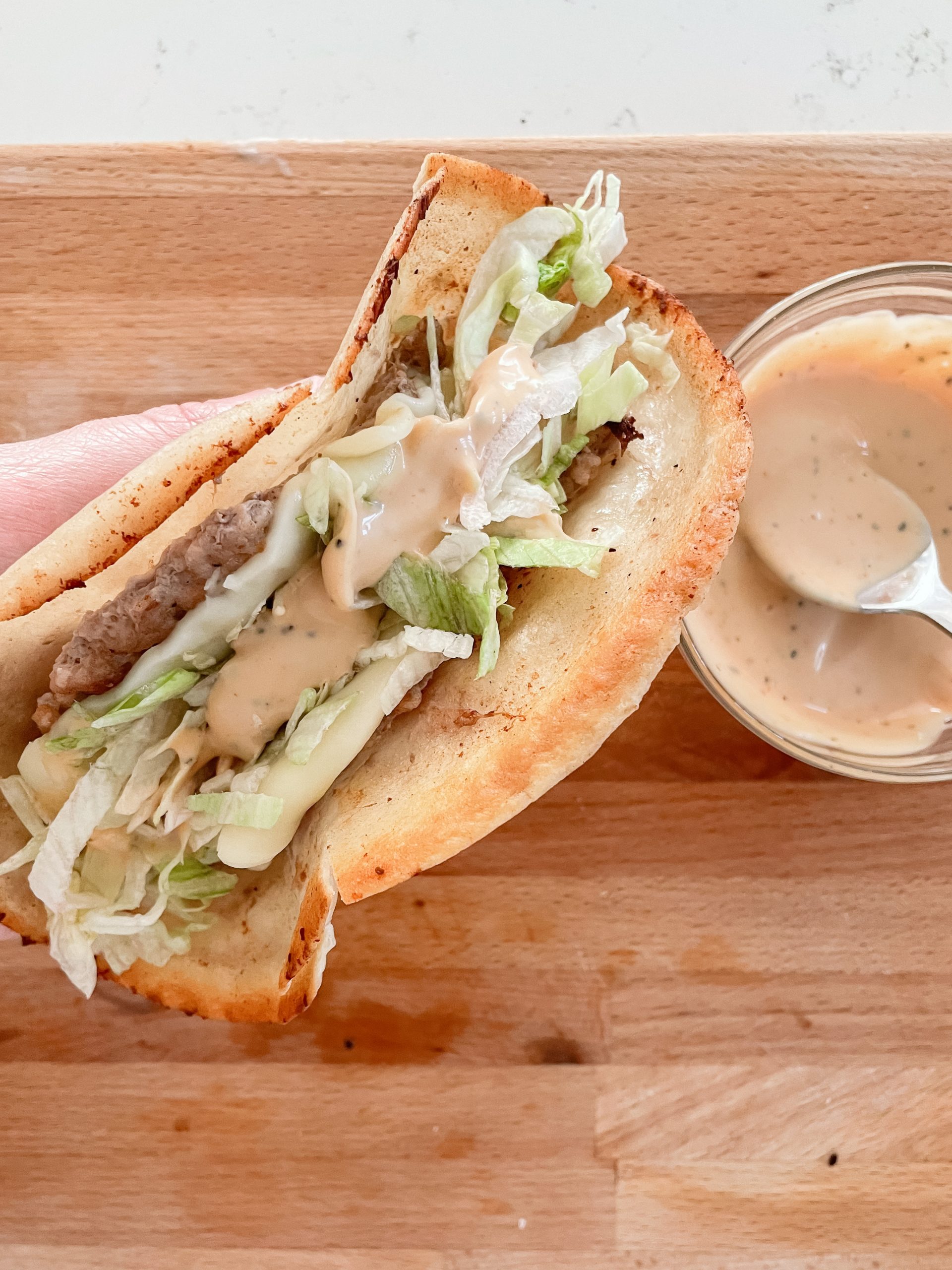 Hand held smash burger tacos, topped with burger sauce and shredded lettuce